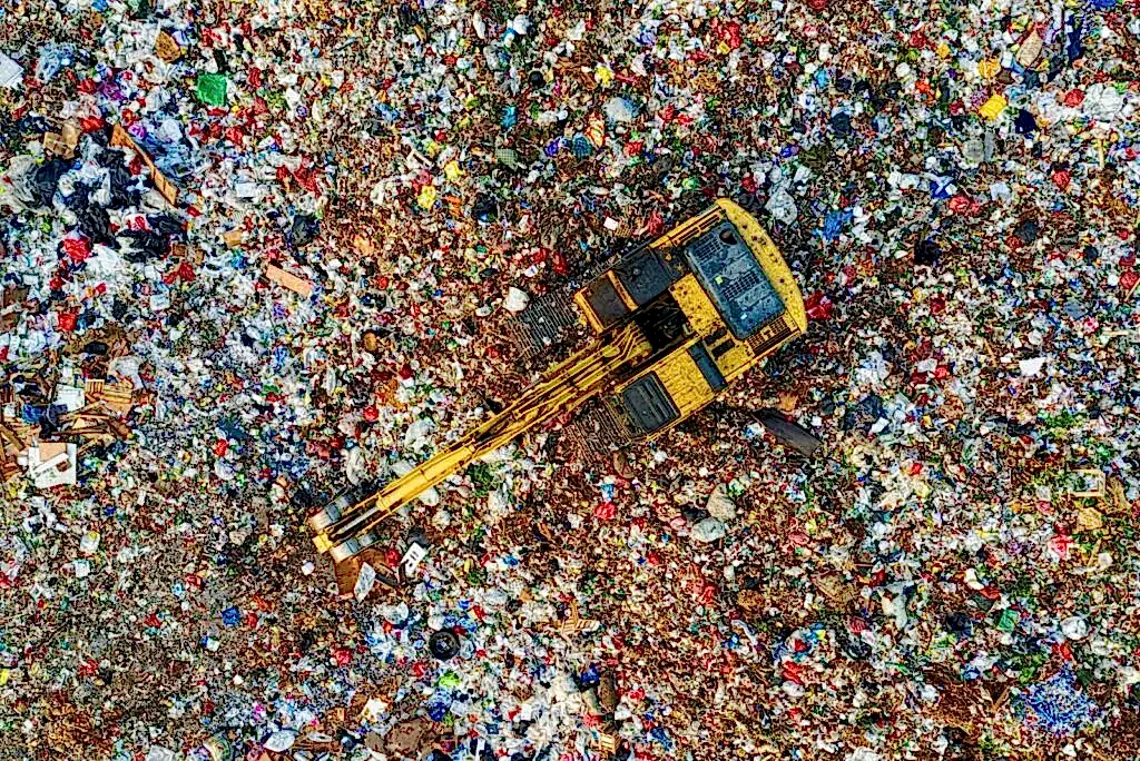 Aerial shot of a landfill with a yellow excavator in South Tangerang, Indonesia.